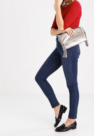 Hopeinen nahkainen olkalaukku, jossa on tupsukoriste. Yhdistetty punaiseen ribbineulottuun toppiin ja tummiin pillifarkkuihin, mustien kiiltävien loafereiden kanssa.