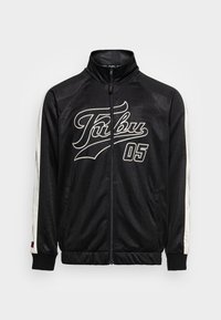 Sort zip-jakke med høj krave, hvide sidelister og "FUBU 05" logo i hvid skrift på fronten. Glat tekstur, moderne design.