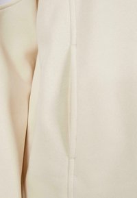 Beige látka s texturovaným povrchem, se švem po boku. Materiál je měkký a mírně elastický, vhodný pro každodenní nošení.