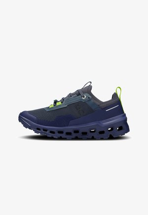 Navy athletic shoes with a textured mesh upper, green accent details, and a thick, ventilated sole featuring cut-out patterns for flexibility.