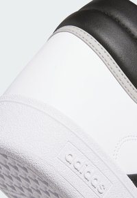 Białe sneakersy z textured (teksturą) podeszwą, czarnymi i szarymi akcentami, górą z gładkiej skóry oraz widocznymi stębnowaniami. Logo wytłoczone na boku.