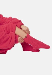 Luddiga rosa strumpor gjorda av mjukt, texturerat material med en nära passform, med en liten brun etikett vid kanten, som kompletterar en matchande filt.