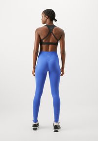 Svart sportbehå med racerback-design, tillsammans med högmidjade, livfulla blå leggings. Båda plaggen är gjorda av mjuk, stretchig tyg.