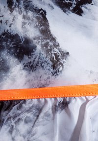 Strukturiertem Stoff mit einem schwarz-weißen Marmor-Muster und einem orangen elastischen Band am unteren Ende. Leicht und halbtransparent.