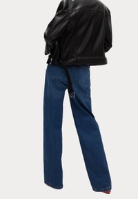 Svart läderjacka med axeldetaljer, kombinerad med blå rakbenade jeans som har fickor och bältesloopar. Slät textur och avslappnad passform.