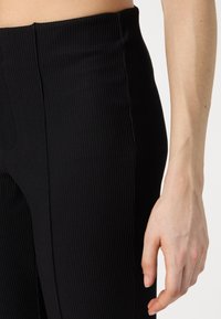 Zwarte geribde leggings met een hoge tailleband, voorzien van een textuurstof en zijnaad. Close-up toont de details van het materiaal.