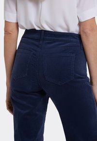 Manchesterbyxor i mörk marinblå, med en mjuk textur, hög midja och två bakfickor med snedställda klaffar.