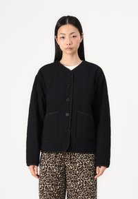 Black quilted jacket with round neck, front buttons, and two side pockets. Features contrasting black trim and textured fabric.