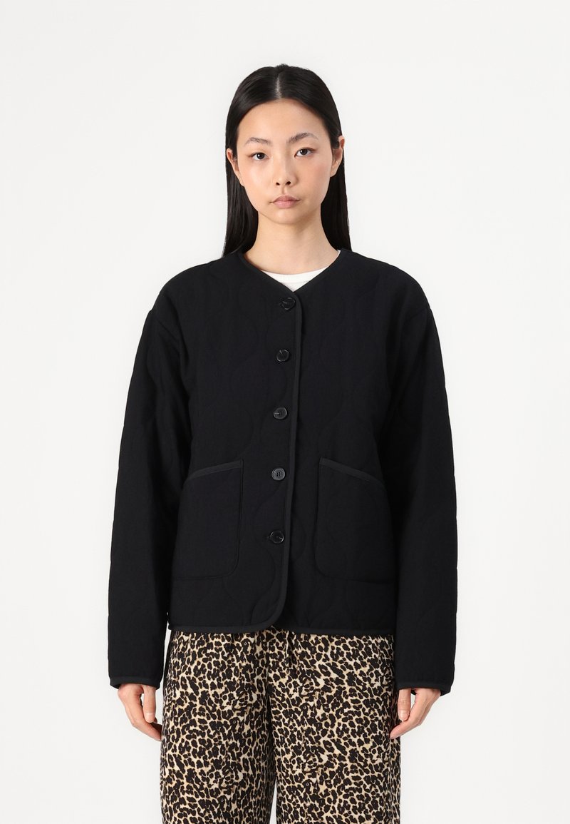 Black quilted jacket with round neck, front buttons, and two side pockets. Features contrasting black trim and textured fabric.