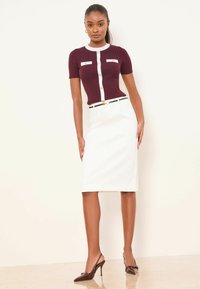 Burgundi punutud ülaosa lühikeste varrukatega ja valgete aktsentidega, kombineeritud valge põlveni ulatuva pliiatsseelikuga ja pruunide kõrgete kontsadega kingadega.