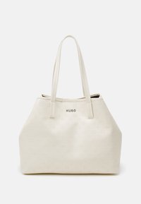 Hvid tote bag lavet af glat materiale med præget logo-mønster. Har to lange håndtag og et diskret mærkeemblem på forsiden.
