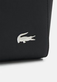 Borsa nera con texture e design elegante, caratterizzata da un accento in argento a forma di coccodrillo. Realizzata in materiale resistente, ha una forma rettangolare.