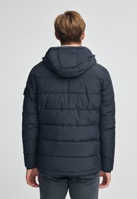 Mörkblå puffjacka med huva, med ett kviltat mönster, elastiska ärmslut och dragkedjestängning. Slät textur och lättviktig.