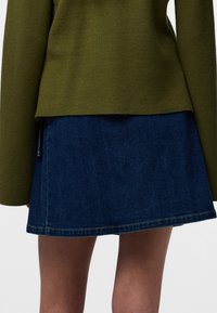 Roheline tekstuuriga kampsun pikkade varrukatega, mida on kombineeritud sinise teksase miniseelikuga. Seelikul on nähtavad õmblused ja see on mõeldud vaba aja kandmiseks.