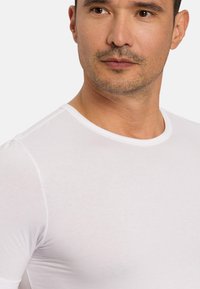 Hvid, tætsiddende T-shirt med rund halsudskæring. Glat tekstur og korte ærmer. Har minimale syningdetaljer.