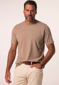 Beige tričko s krátkým rukávem, bavlněná tkanina, kulatý výstřih, nošeno s krémovými kalhotami a hnědým koženým opaskem, doplněno hodinkami.