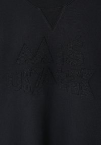 Czarna bluza z miękkiego materiału, z teksturowanymi, wypukłymi czarnymi literami i geometrycznymi kształtami na przodzie oraz prążkowanym kołnierzem.