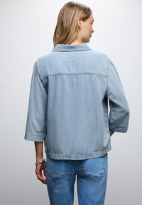 Giacca di jeans azzurro chiaro con vestibilità comoda, maniche tre quarti e colletto classico. Sul retro presenta una cucitura a yoke e dettagli cuciti.