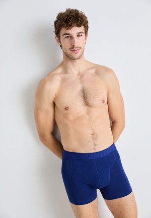 Boxer da uomo blu navy con elastico in vita e scritte in rilievo. Texture liscia, lunghezza a metà coscia e design aderente.