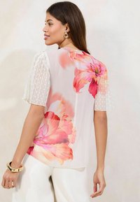 Floral blouse with a white lightweight fabric, featuring pink and orange flower prints. Puff sleeves with textured polka dots. Smooth finish.