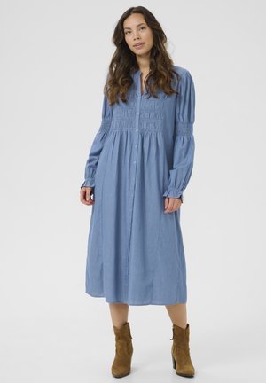 Light blue button-down dress with long sleeves, gathered details at the bodice, and a flowing A-line silhouette. Styled with brown ankle boots.