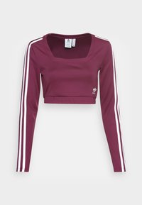 Burgundy dlouhý rukáv cropped top s čtvercovým výstřihem. Obsahuje bílé pruhy podél rukávů a malé logo na spodní straně. Hladká textilie.