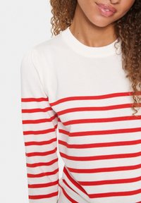 Maglione lavorato a maglia a righe rosse e bianche con scollatura a girocollo e polsini a costine. Il tessuto appare morbido con una leggera texture.