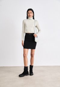 Gaiši beigu pieskares topi, pieguļošs turtlenecks; melna, ķermeņa formas mini svārki; teksturētas melnas potīšu zābaki ar apakšu; krustota soma gaiši pelēkā krāsā.