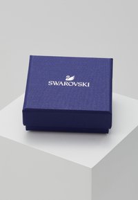 Swarovski jewelry box in deep blue textured paper with a white logo featuring a swan. Rectangular shape with a smooth finish.