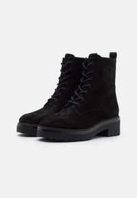 Bottines en daim noires avec un bout rond, un laçage et une surface texturée. Semelle épaisse avec un léger détail de couture et une languette au dos.
