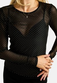 Čierny priehľadný top s dlhými rukávmi, zdobený zlatými bodkami a hlbokým výstrihom do tvaru písmena V. Hladká textúra s priliehavým strihom.
