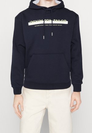 Sweat à capuche bleu marine avec poche à l'avant et texte « Denim Tom Tailor established two thousand seven » porté avec un pantalon beige clair.