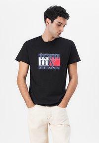 T-shirt en coton noir avec un grand logo multicolore "tommy JEANS" sur le devant. Manches courtes et coupe standard.