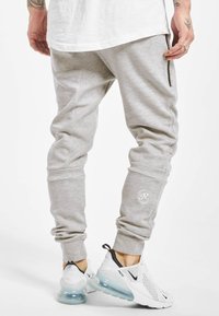 Light gray jogger pants with elastic cuffs and side zip pockets. Features a logo on the lower leg and a soft, textured fabric.