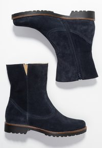 Námornické semišové kotníkové boty se zipem na boku, strukturovaným povrchem, odolnou gumovou podrážkou a kontrastním hnědým lemem podél okraje podrážky.