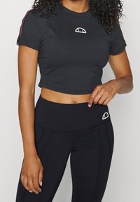 Top atlético negro corto con mangas cortas, que presenta un pequeño logo blanco en el pecho y franjas de acento rosa en los hombros.