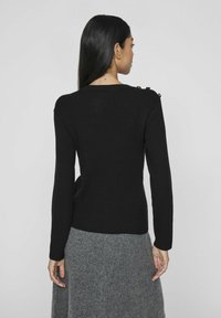 Pull noir côtelé avec des manches longues et des accents de boutons sur l'épaule, associé à une jupe grise. La texture semble douce et ajustée.