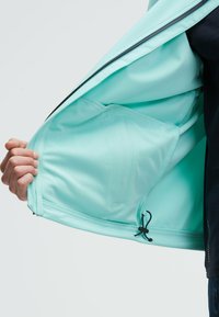Giacca leggera di colore verde menta con un'esterno liscio e foderatura in rete. Caratterizzata da chiusura con zip, orlo regolabile con cordino e tasca interna.