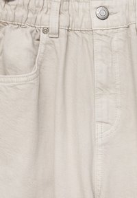 Pantalons en coton léger beige avec une taille élastique, une poche avant et un accent en bouton argenté. Texture lisse et design décontracté.