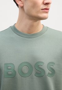 Felpa verde in cotone con collo a giro, caratterizzata da un logo "BOSS" in rilievo della stessa tonalità e con una texture liscia.