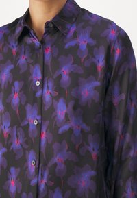 Schwarze Bluse mit lila und roten Blumenmustern, Knopfverschluss vorne, klassischer Kragen, lange Ärmel, glatte Textur.
