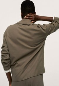 Sudadera color caqui con un ajuste relajado, que presenta un cuello doblado y mangas largas, mostrada desde atrás. Textura suave, diseño casual.