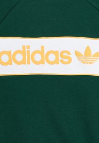 Grön sweatshirt med ett brett vitt band med gul "adidas"-text och logotyp. Mjuk tyg, ribbad halsringning och en ren design.