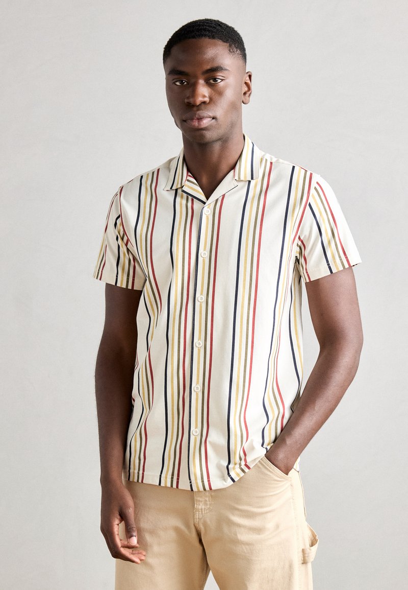Chemise à manches courtes avec des rayures verticales en rouge, jaune et bleu sur un fond crème, dotée d'une fermeture à boutons et d'un col.