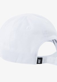 Bela kapa s sledičem, izdelana iz teksturirane tkanine. Ima ventilacijska okna in črno nastavljivo zaponko z oznako na hrbtni strani.