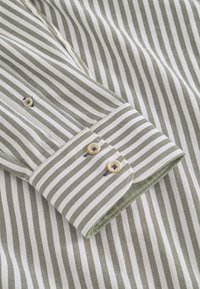 Polsino della camicia a righe con righe alternate di verde oliva e bianco, dotato di due chiusure con bottoni e fodera interna a contrasto.