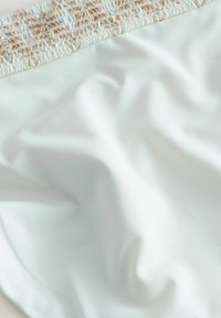Ljusblått tyg med en strukturerad, vävd beige midjeband. Materialet verkar slätt och något elastiskt, vilket visar på mjuka draperingar.