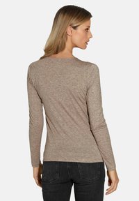 Langärmliges beiges Oberteil aus weichem Stoff, mit Rundhalsausschnitt und figurbetontem Design, von hinten gegen einen schlichten Hintergrund betrachtet.