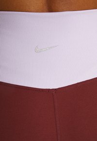 Hoge taille legging met brede geribde lavendel tailleband en een diep bordeauxrode onderkant. Bevat een klein, pastel Nike-logo.