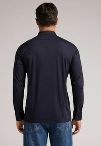 Mörkblå långärmad skjorta med en subtil lyster, strukturerad krage och knäppta manschetter; slät textur; bärs med denimjeans.